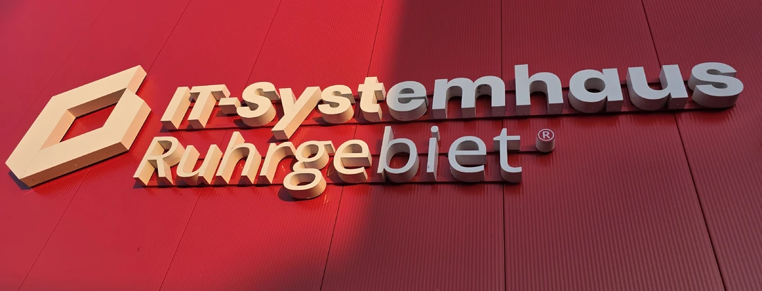 Signage of IT-Systemhaus Ruhrgebiet displayed on a red wall, showcasing the company name in a modern font.