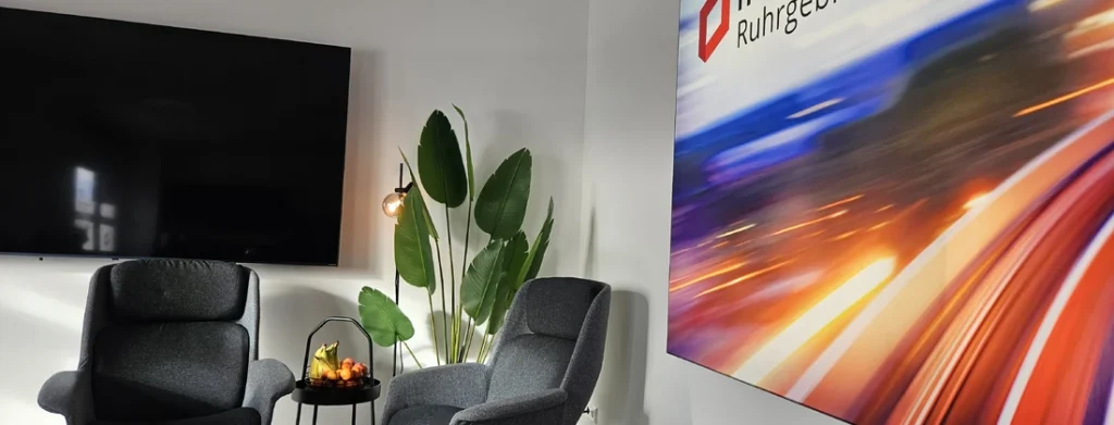 Zwei graue Sessel mit einem kleinen Tisch und einer Pflanze in einem modernen Raum mit einem Fernseher und einem großen Wandbild.