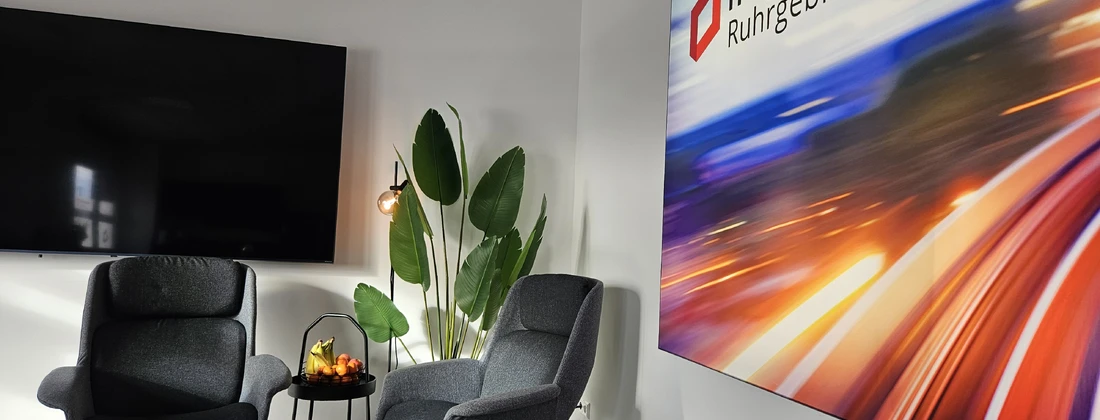 Zwei graue Sessel mit einem kleinen Tisch und einer Pflanze in einem modernen Raum mit einem Fernseher und einem großen Wandbild.