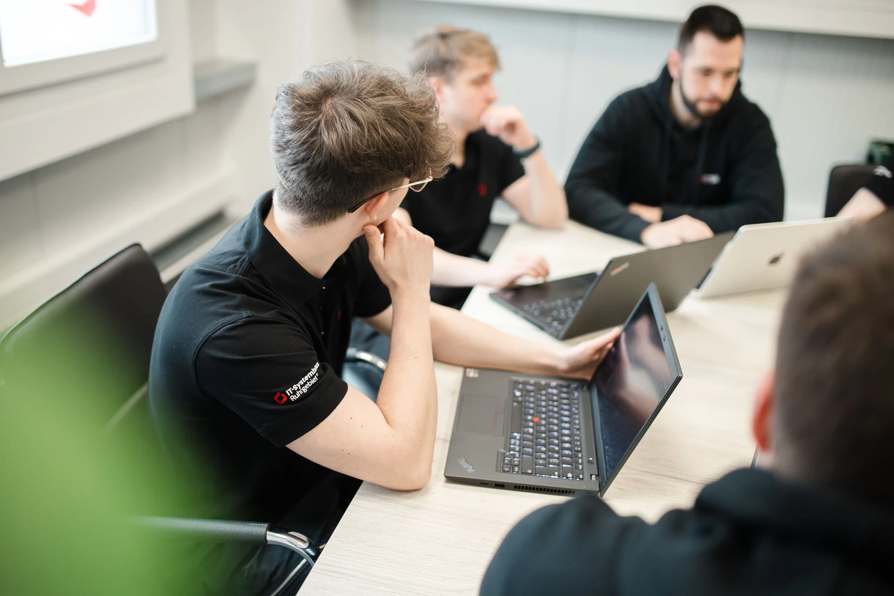 Mitarbeiter in schwarzer Kleidung mit Laptops in einem Besprechungsraum bei IT Systemhaus Ruhrgebiet.