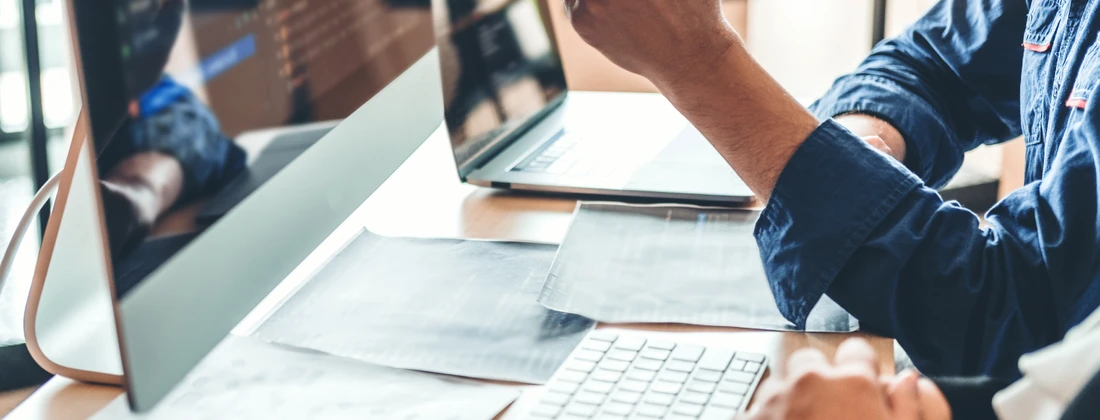 Person, die an einem Computer arbeitet, während sie mit einer Hand auf den Bildschirm zeigt.