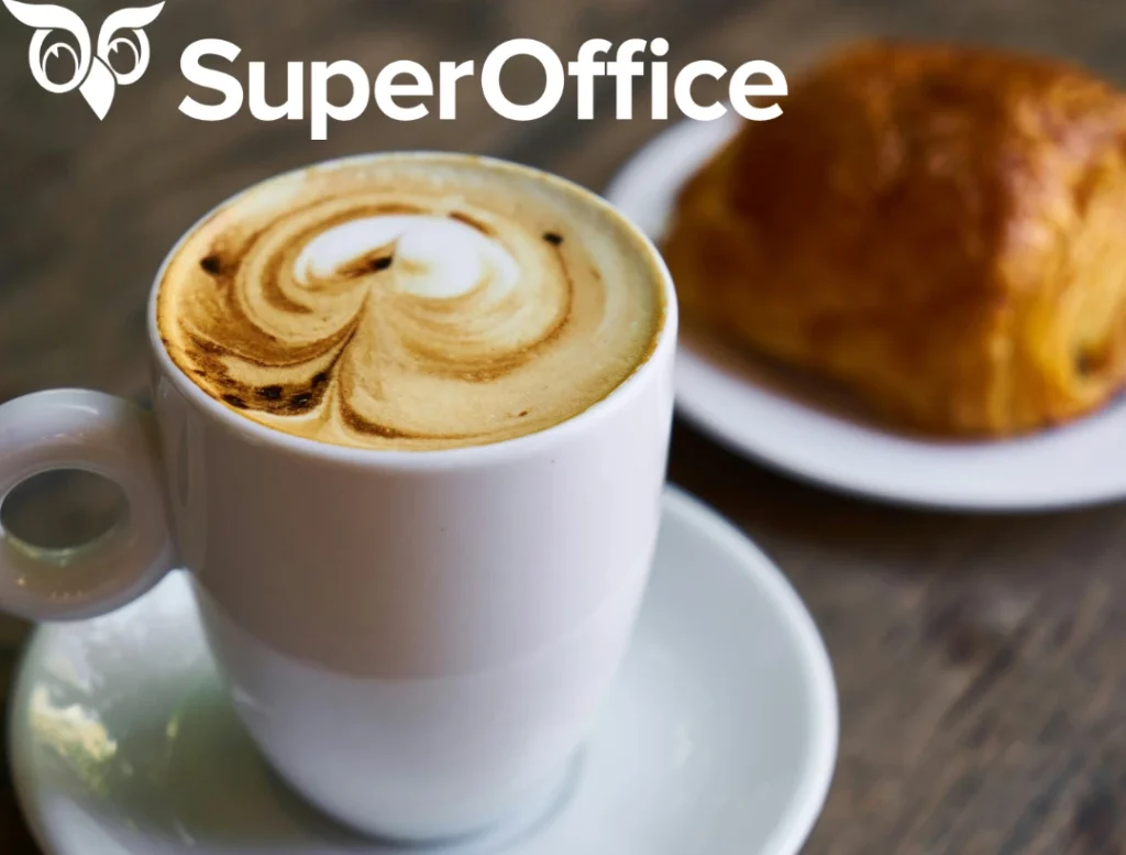 Tasse mit Kaffee und kunstvollem Milchschaum neben einem Croissant auf einem Teller.