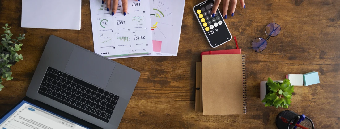 Arbeitsplatz mit Laptop, Smartphone, Notizbuch und Diagrammen auf einem Holztisch.