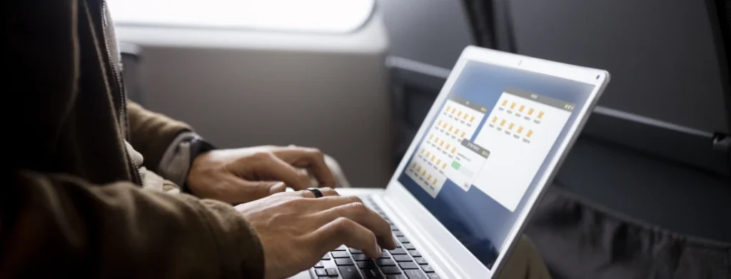 Person, die auf einem Laptop in einem Transportmittel arbeitet, mit geöffneten Ordnern auf dem Bildschirm.