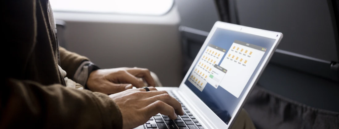 Person, die auf einem Laptop in einem Transportmittel arbeitet, mit geöffneten Ordnern auf dem Bildschirm.