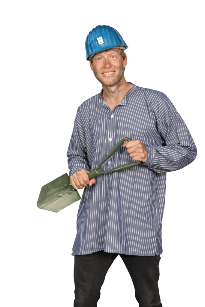 Mann mit blauer Bauhelm und gestreiftem Hemd, der eine Schaufel in der Hand hält.
