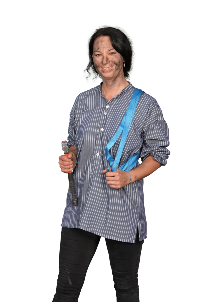 Frau mit einem blauen Tragegurt und einem Werkzeug in der Hand, bekleidet mit einem gestreiften Hemd.