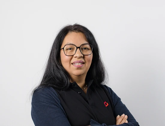 Frau mit langen schwarzen Haaren und Brille, die in einem schwarzen Hemd mit rotem Logo posiert.