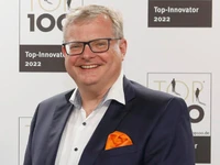 Thomas Ekkehard lächelt in einem Anzug mit einer orangefarbenen Tasche auf einer Veranstaltung für Top-Innovatoren 2022.