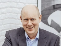 Guido Dreymueller lächelt in einem Anzug mit einem hellblauen Hemd vor einer hellen Wand.