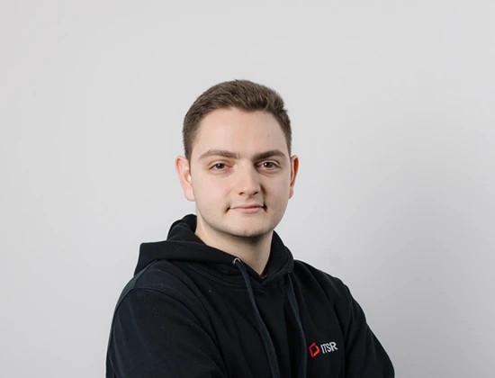Junger Mann mit einem schwarzen Hoodie, der das Logo von ITSR trägt, steht mit verschränkten Armen vor einem neutralen Hintergrund.