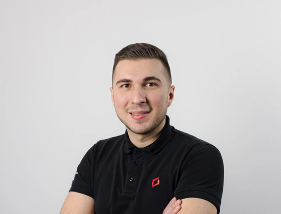 Semir in einem schwarzen Poloshirt mit gekreuzten Armen vor einem neutralen Hintergrund.