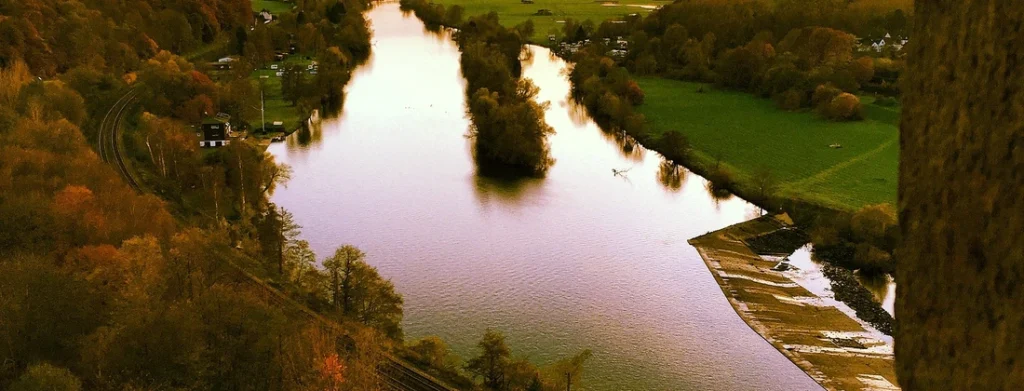 Flusslandschaft mit ruhigem Wasser und Bäumen entlang des Ufers in der Herbstsaison.